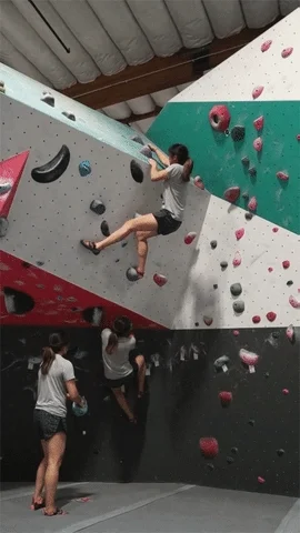 A woman climbs up a wall using a specific beta to solve the wall's problem.