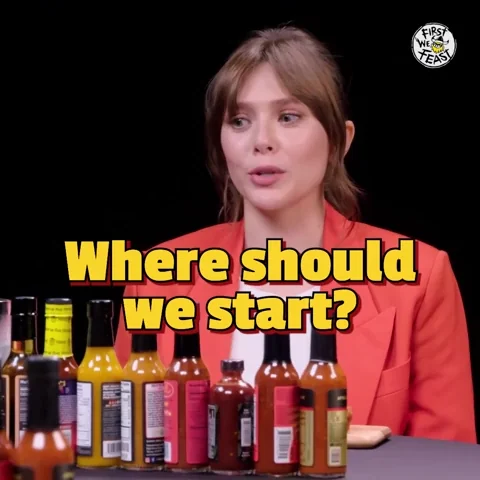 Elizabeth Olsen looks at bottles of hot sauce. She says, 