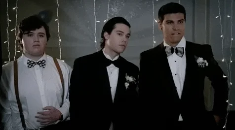 Three young men at a prom checking their phones.