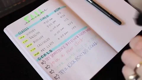 A person writing their class schedule and goals in a journal.
