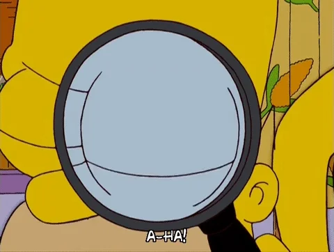 Homer Simpson uses a magnifying glass. The caption reads 'A-ha!'