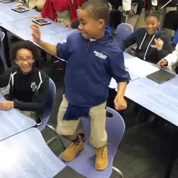 A kid dancing on a chair in a classroom.