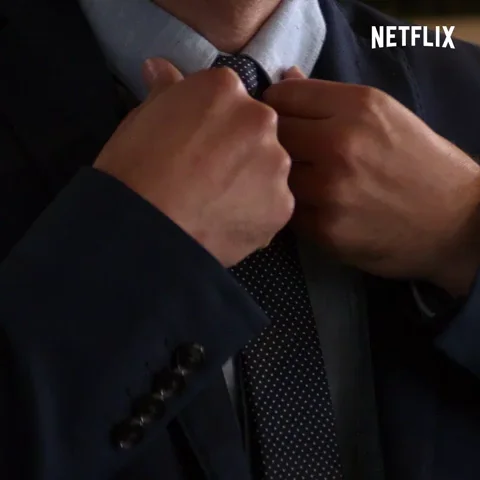 A GIF of man checking his teeth in a spoon,fixing his tie and wrist buttons, and licking his eyebrows with his fingers
