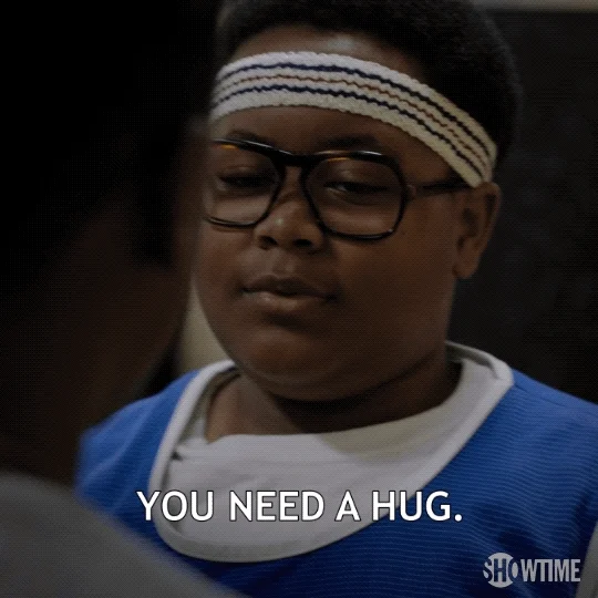 A child dressed in a gym uniform and headband tells their friend 'You need a hug.'