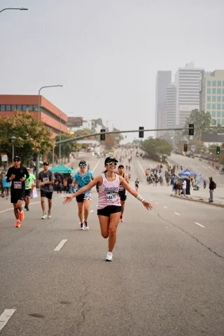 A smiling woman runs a marathon with arms outstretched, celebrating