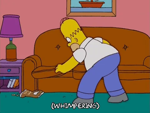 Homer Simpson searching the couch cushions for something and whimpering.