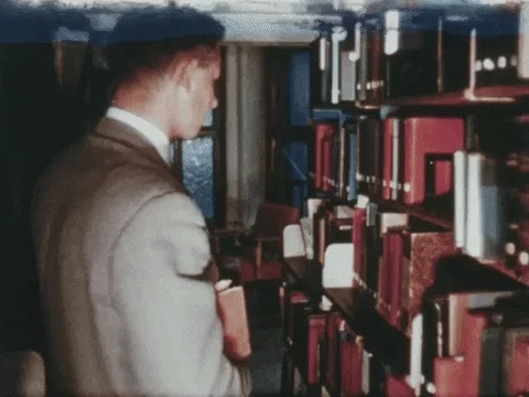 A student picking up a book from a library shelf to read. 