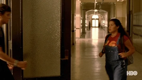 In a college hallway, a girl walks by a guy and the guy looks backs at her.