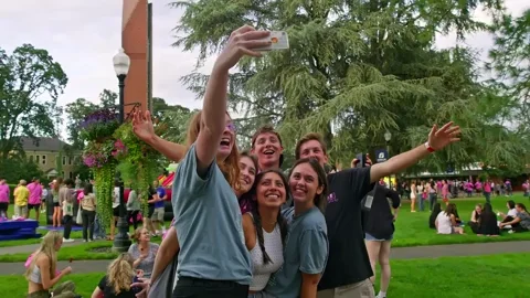 A group of college students taking pictures together on a campus field.