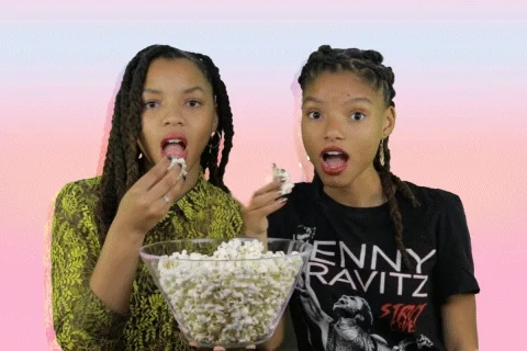 Two young women sit together, captivated, eating popcorn.