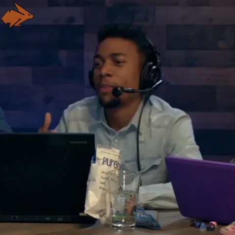 A man sitting at a computer wearing headphones, gesturing toward his screen and saying, "Let me just show you."