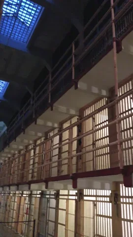 Two rows of empty jail cells with closed barred doors, stacked on top of each other.