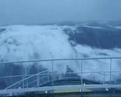 A ship in the ocean. A wave crashes into it during a storm.
