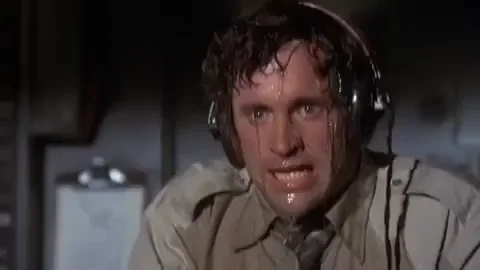 A man with sweat dripping all over his face. He looks scared and is wiping his eyes. 