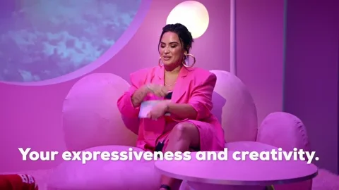 Demi Lovato sits in a pink room while wearing a pink suit. She says, 