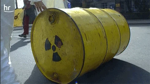 Nuclear plant workers in hazmat suits rolling radioactive barrels.