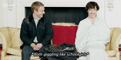 Sherlock and Watson sitting on a couch laughing