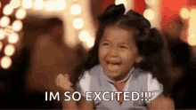 Young girl raising both arms with fists balled with a smile on her face saying 'I'm So Excited!!!'