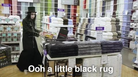A goth couple shopping at Bed Bath and Beyond argue about whether a black bath mat can work as a living room rug.