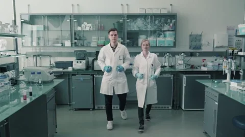Two scientists walking in a lab while holding pipettes. The text reads: 