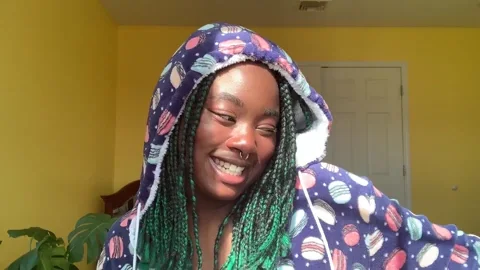 A woman in her bedroom holds up a journal, smiles, and shimmies enthusiastically.