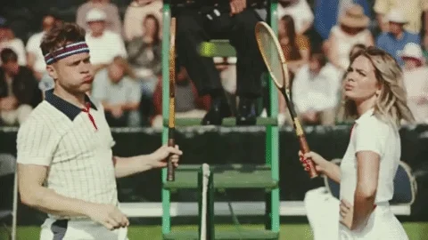 Two tennis players exchange volleys across a net. One looks at his watch, while the other raises her hand and yawns.