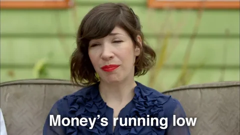 Two people sitting on a couch outside a house. One says, "Money's running out." The other responds, "Not my fault."