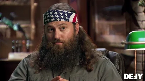 A man with long beard and an American flag headband with the text 'Trust Me' 