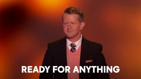 The game-show host Ken Jennings in a dark suit jacket and pink sweater vest. He says, 
