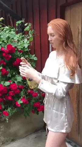 A young woman in a garden opening a champagne bottle. It sprays in her face.