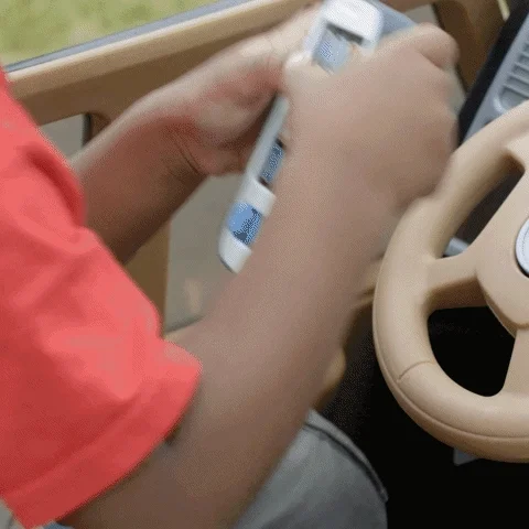 GIF of boy sitting in a toy car and throwing his phone onto the lawn