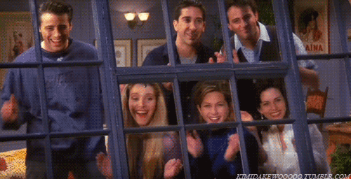 The cast of Friends looking through an apartment window while applauding.