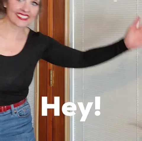 A woman in an office waves and smiles.