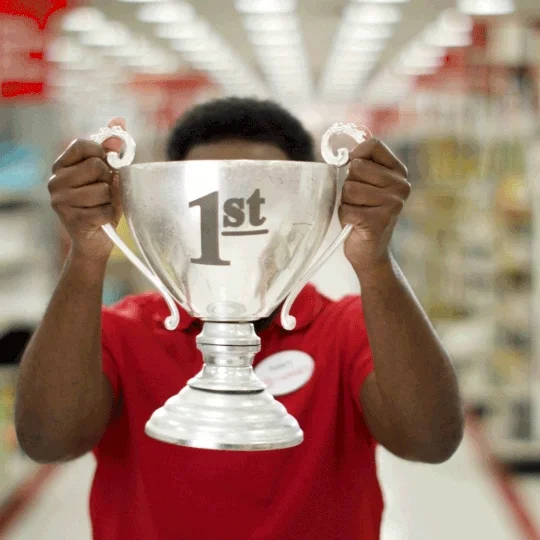 A man in a red shirt is hiding his face behind a large silver cup that says 