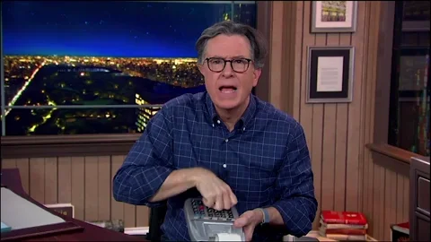 A GIF of Stephen Colbert tapping multiple buttons on a large calculator.