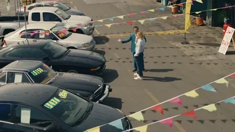 A salesman selling a car at a dealership parking lot.