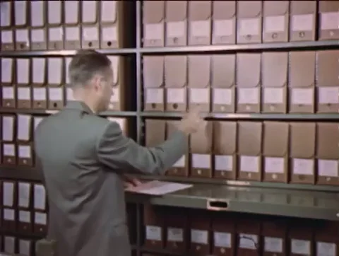 Old footage of a man reviewing a file in an archive.
