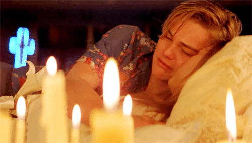 Romeo hugging Juliet as she lies unconscious beside candles.