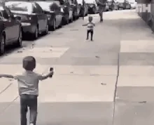 Two toddlers with open arms running towards each other for a hug on the sidewalk. 