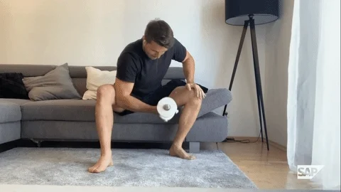 Man sitting on couch lifting a weight in one hand. The dumbells have been replaced with toilet paper rolls.