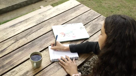A woman sitting at a park bench and writing in her journal.