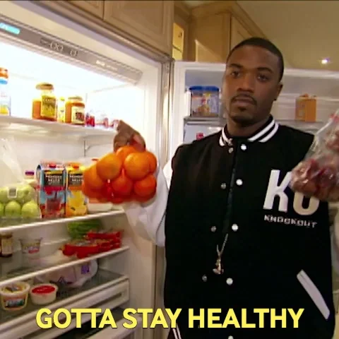 A man standing in front of open refrigerator holding bags of oranges and grapes. The caption reads, 
