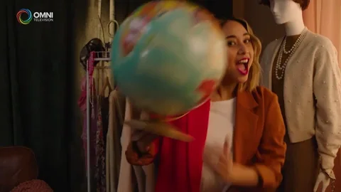 A woman saying 'we're going abroad' while winking and spinning a globe.