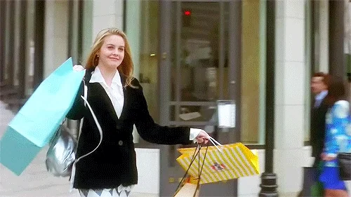 Alicia Silverstone excitedly walks while carrying multiple shopping bags.
