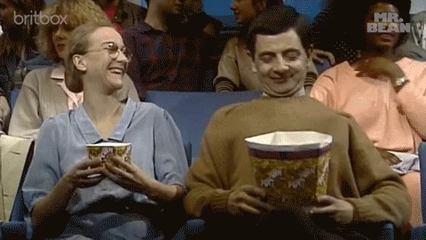 TV character Mr. Bean stops a friend from taking popcorn from his large popcorn container at the movie theater.