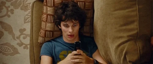 A top down view of a young man laying on a couch as the camera zooms away. Images of people he's communicating with appear.