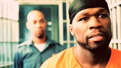 A corrections officer walking behind rapper 50 Cent in a prison hallway.