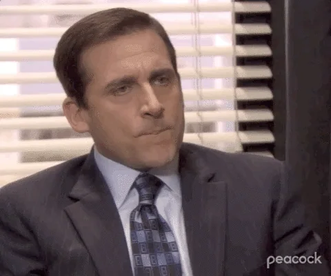 Michael Scott from The Office raises his eyebrows with a confused expression. He says, “What?”