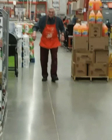 A male employee, wearing an orange Home Depot apron, dancing in a crowded aisle.