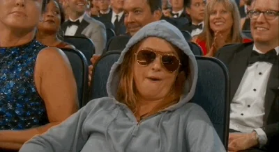 A woman sitting comfortably at an award show, chewing gum and flashing victory signs.
